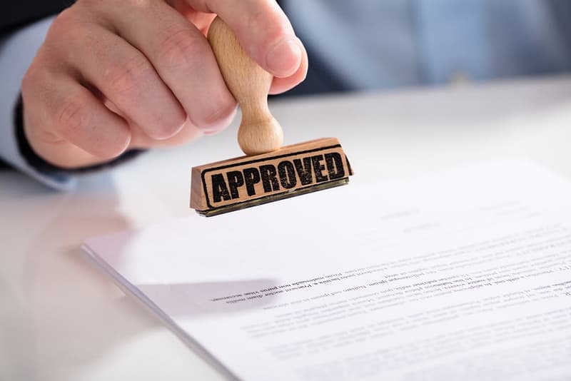 A man holding a rubber stamp with the word approved on it at a Year-Round Campground, giving Greenlights by the Anderson County Board.