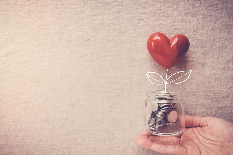 A hand holding a jar of money with a heart in it at one of the Wisconsin Campgrounds.