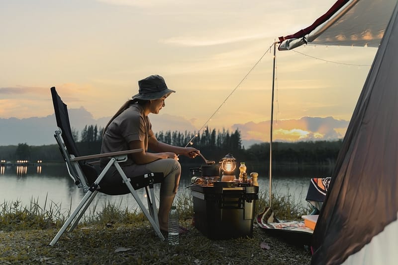 At sunset, a woman sits in front of a tent, creating an idyllic scene for outdoor recreation.