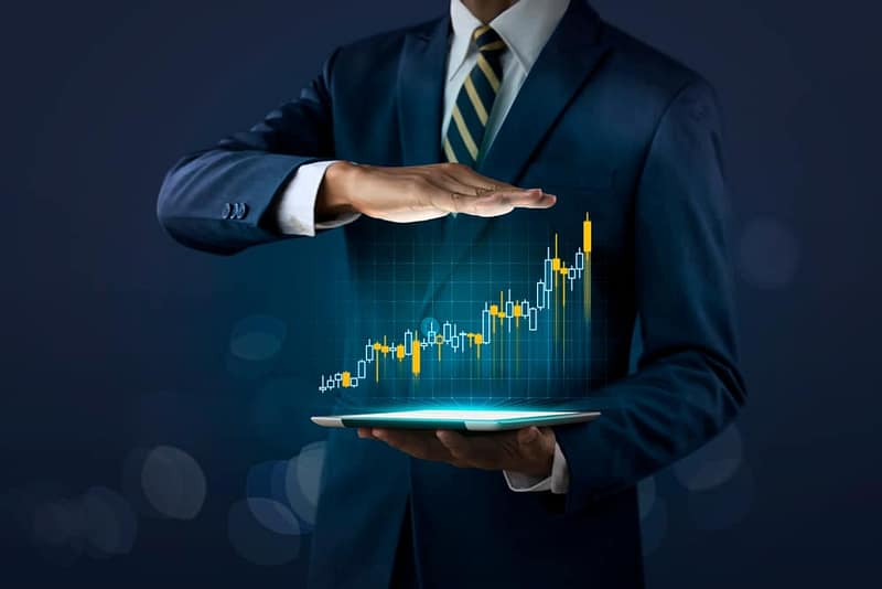 A businessman holding a tablet with a stock chart on it, showcasing the impressive growth of CRR Hospitality, ranked on the Inc. 5000 list.