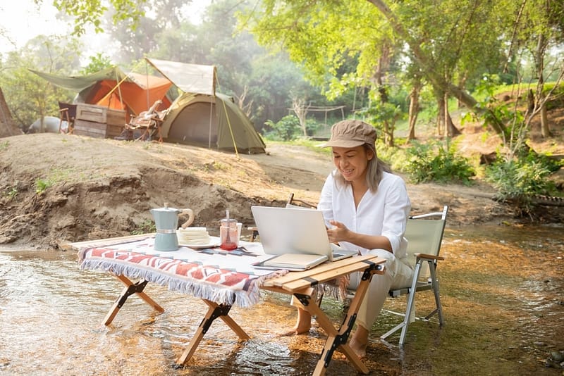 A woman working on her laptop at a campground near a tent.