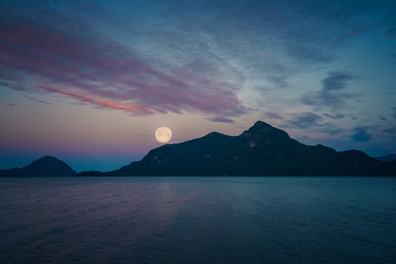 A full moon rising over Porteau Cove, a proposed campground situated by a serene body of water and majestic mountains.