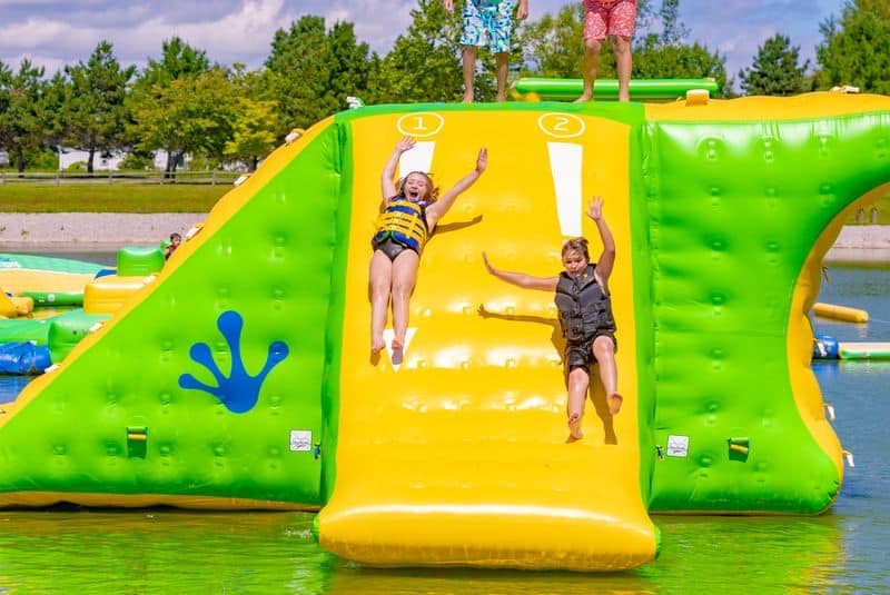 Two children sliding down a large inflatable water slide, with a third child's silhouette imprinted on the slide, set against an auto draft backdrop.