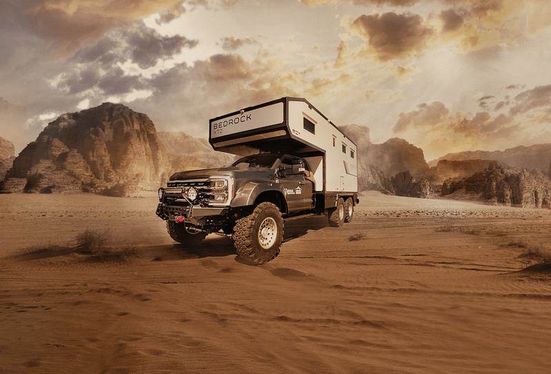 A rugged off-road camper truck, looking like an auto draft from an adventure novel, drives through a desert landscape with rocky cliffs and a dramatic sky in the background.