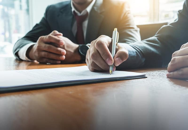 Two businessmen signing a document at a desk.