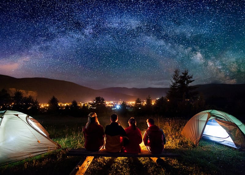 Last-Minute camping on July Long Weekend, a group of people sitting around a campfire under a starry sky.