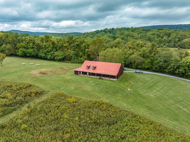 Aerial view of a large red-roofed building in Sweet Run State Park, surrounded by a green landscape with trees and a cloudy sky.