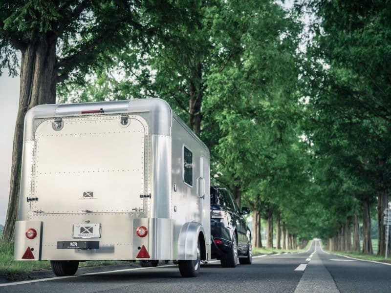 An Innovative Caravan Salon on wheels, equipped with a spotlight, steadily travels down a scenic country road.