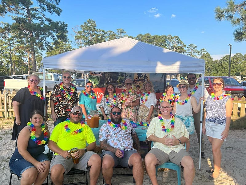 A group of people posing under a tent at the Business After Hours networking event on the beach.