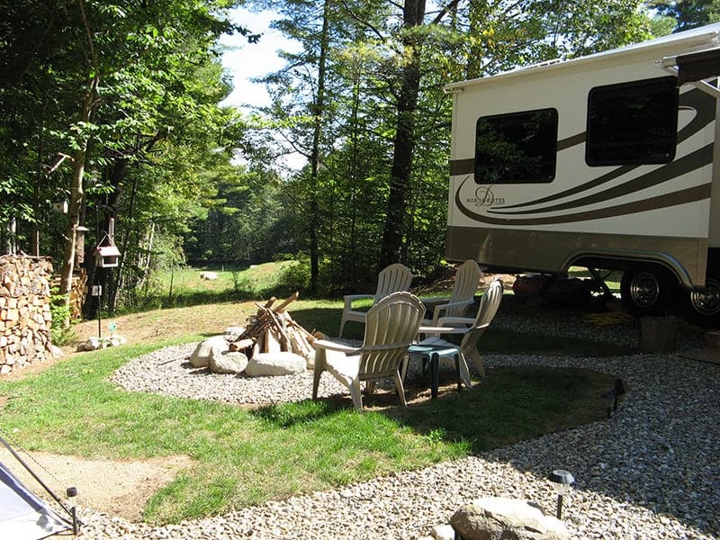 An RV parked in a wooded area with a fire pit at Loon Lake RV Park.