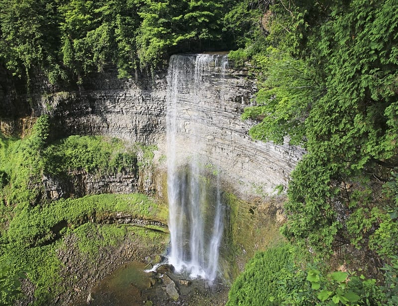 An aerial view of a waterfall in a green forest surrounded by Campgrounds.