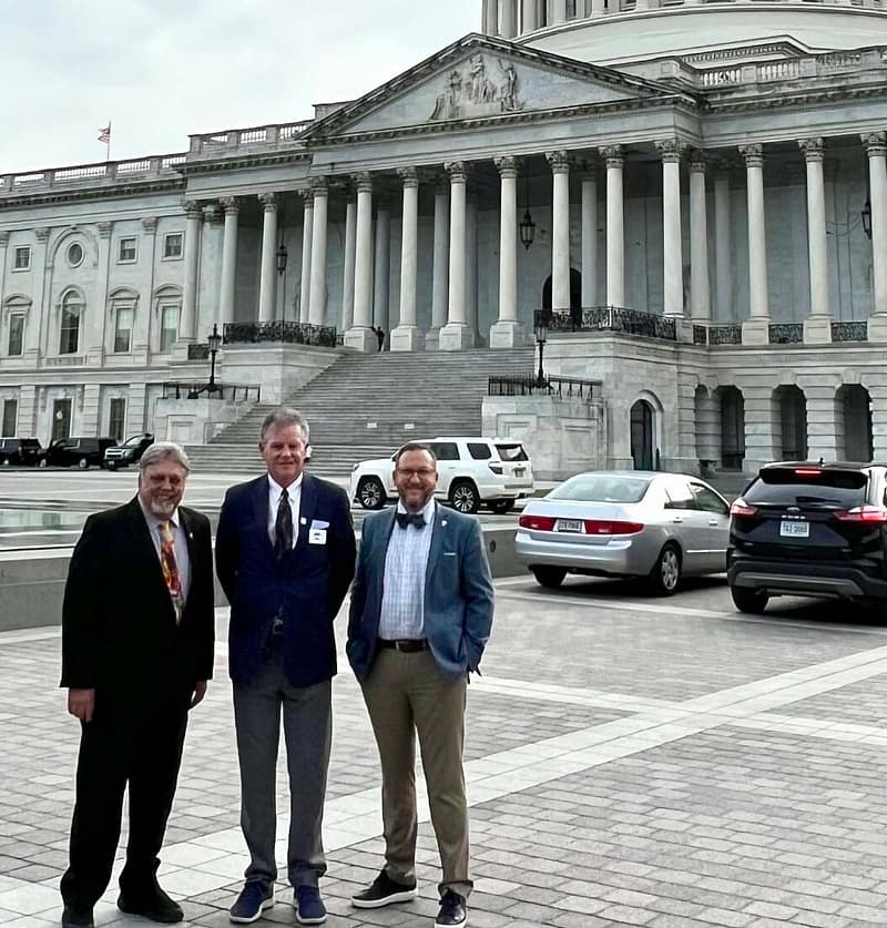 Three men standing in front of the United States Capitol building on a cloudy day.