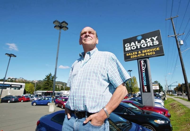 The owner of Galaxy Motors standing in front of his car dealership.