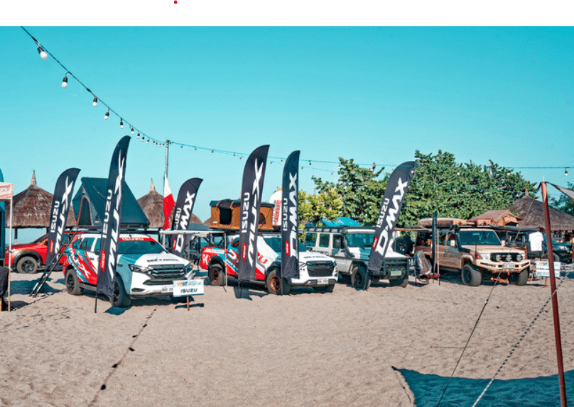 A group of Isuzu D-MAX trucks parked on the beach with banners for Overlanding Philippines.
