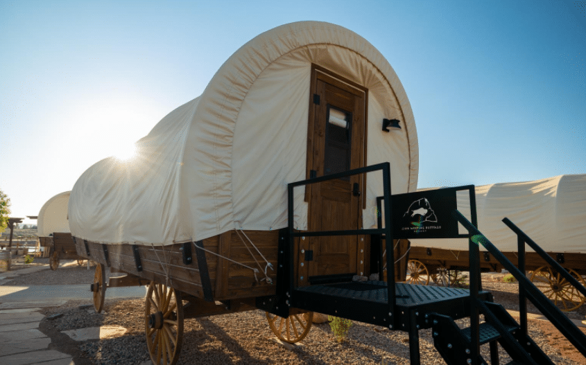 A glamping covered wagon is parked in a parking lot.