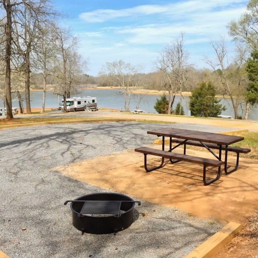 The Skull Island Campground reopens with a picnic table and fire pit in front of a serene lake.