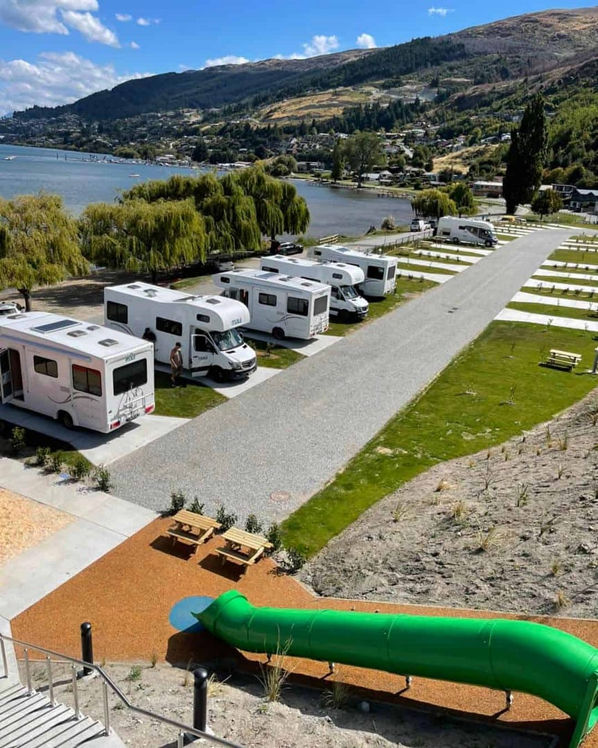 A group of campervans parked next to a lake in Queenstown campground.