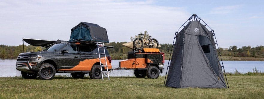 An off-grid Ford Expedition SUV is parked next to a Timberline tent.