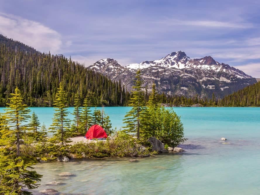 A red tent sits on a small island in a turquoise lake, offering Camping Reservations for BC 2023.