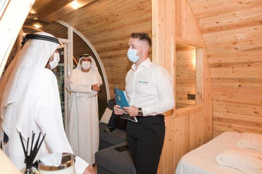 Two men wearing face masks inside a portable luxury glamping pod designed by Glampitect in a wooden cabin.