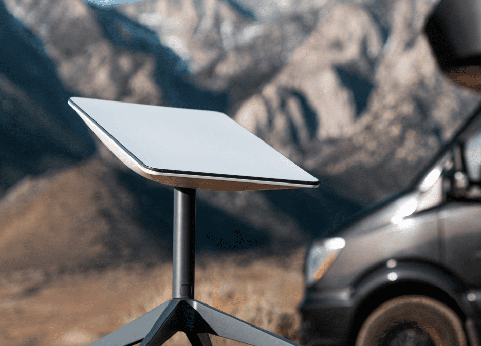 A SpaceX satellite dish sits on top of a table in front of mountains, providing Starlink internet services.