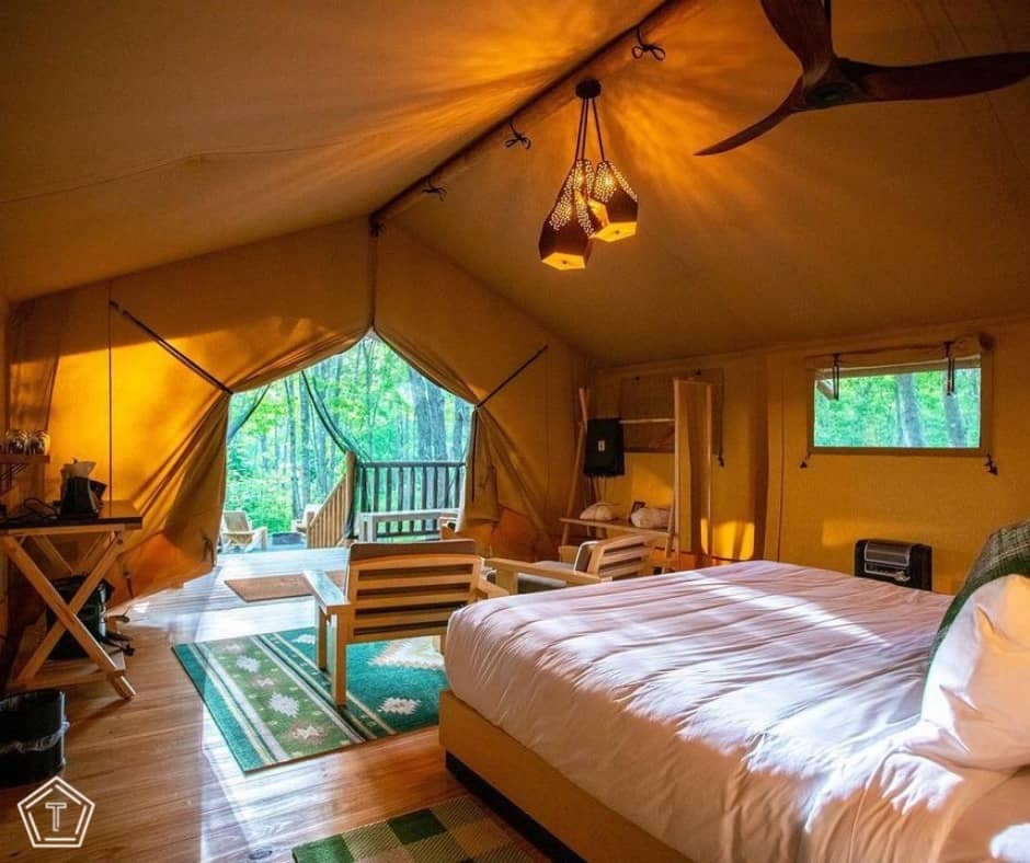A bedroom in a tent at a Glamping Resort in Maine, complete with a cozy bed and a convenient bedside table.