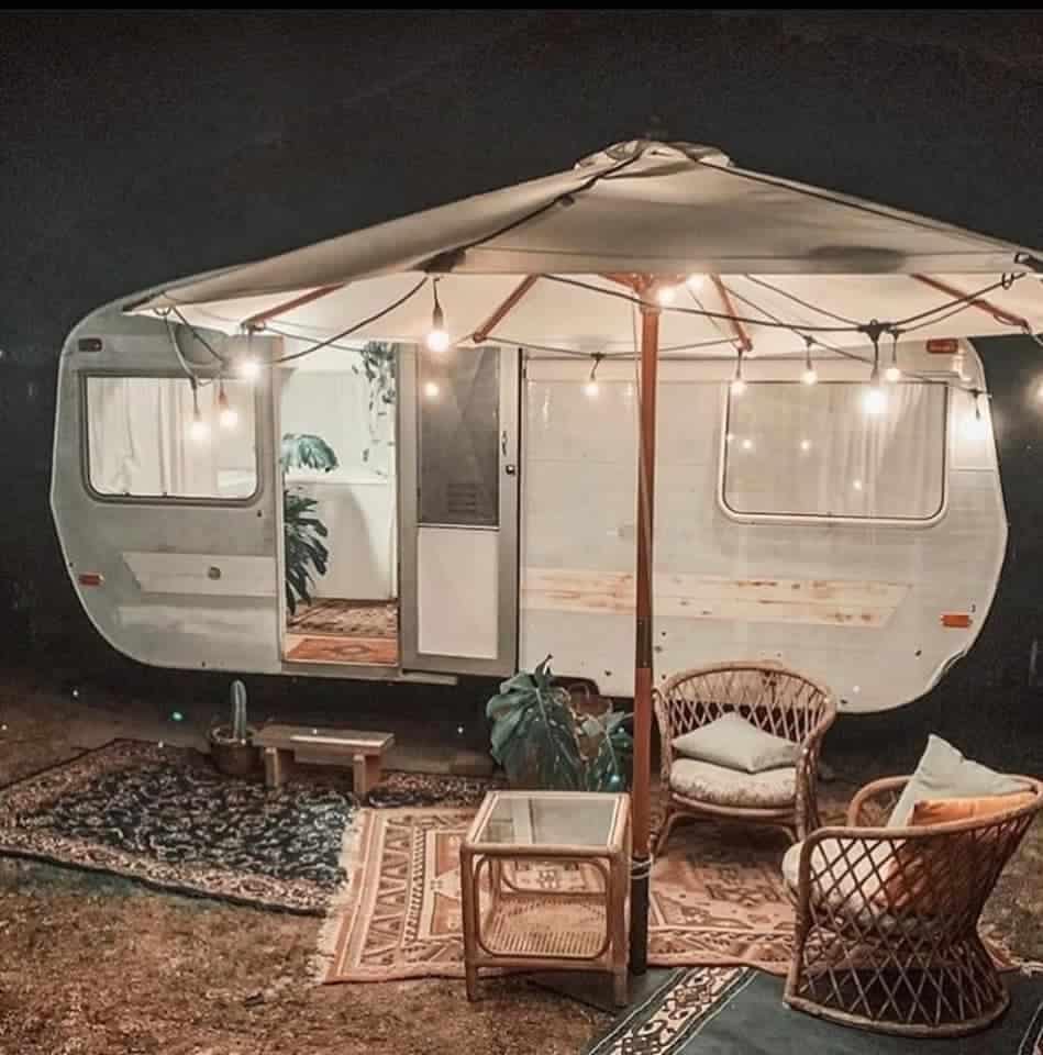 A glamping caravan equipped with furniture and an umbrella, perfect for a luxurious camping experience in Malaysia.