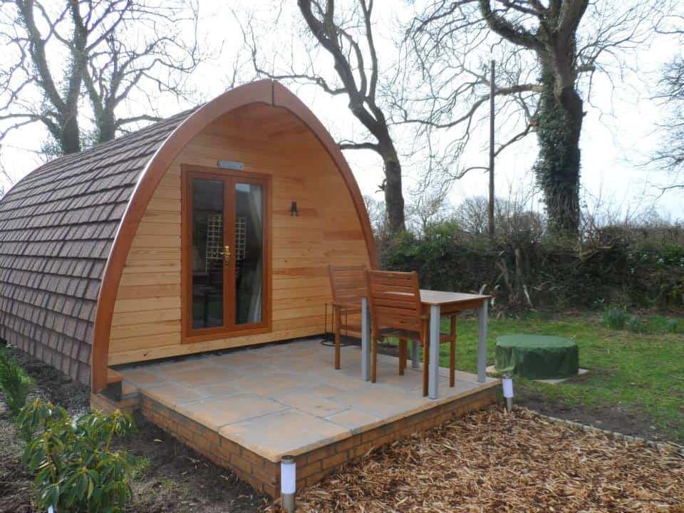 A small wooden cabin for sale in the UK, perfect for a glamping retreat with a table and chairs.