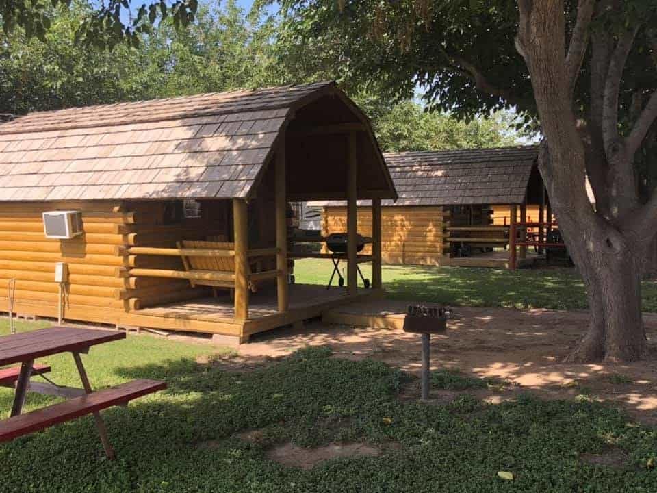 Two small cabins with picnic tables in the yard, now under new ownership at Midland/Odessa KOA Journey.