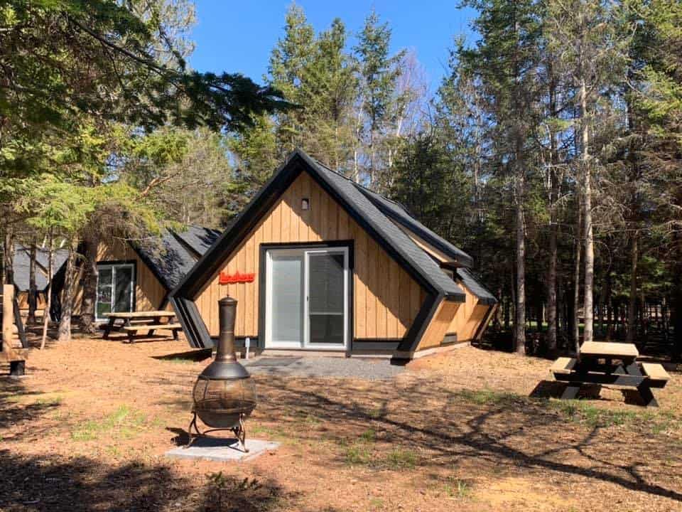 A cozy cabin, perfect for nature lovers seeking a PEIs glamping retreat. The cabin is nestled in the peaceful woods and features a picnic table for outdoor dining.