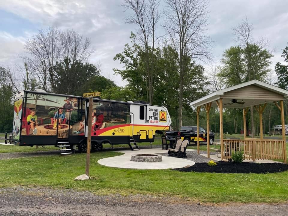 Located at the Medina/Wildwood Lake KOA, this virtual campground tour showcases an RV parked in a park with a fire pit.