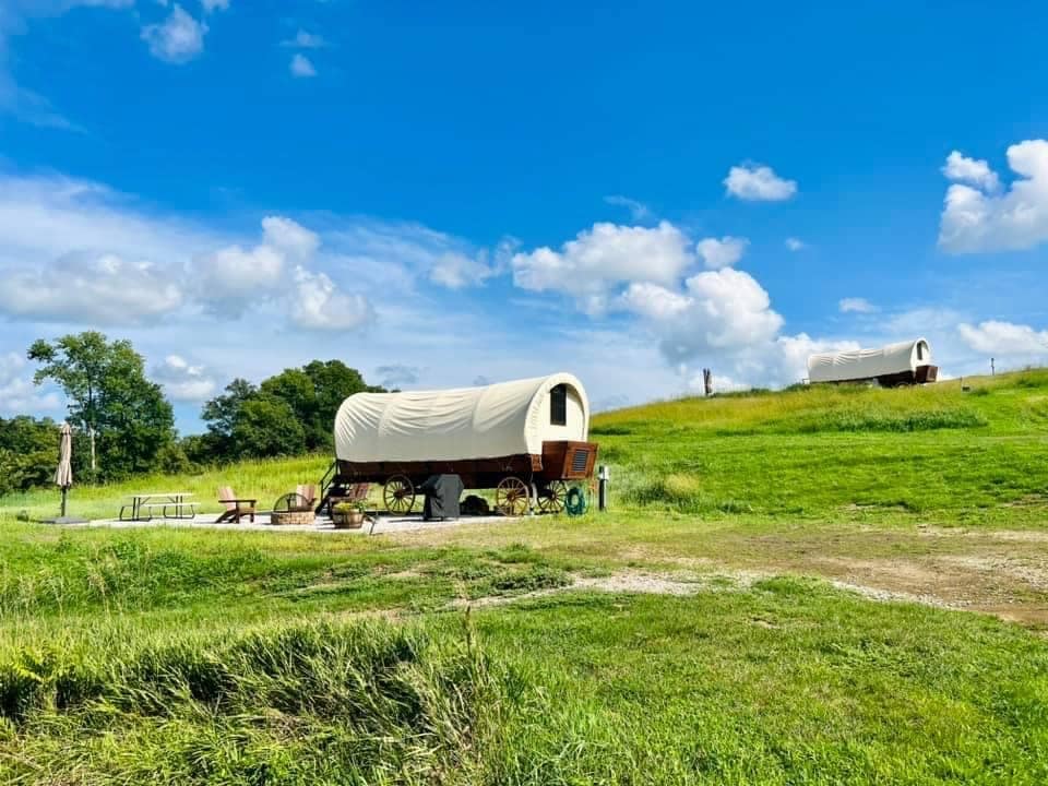 Two luxury covered wagons sit on a grassy hill in Mills County.