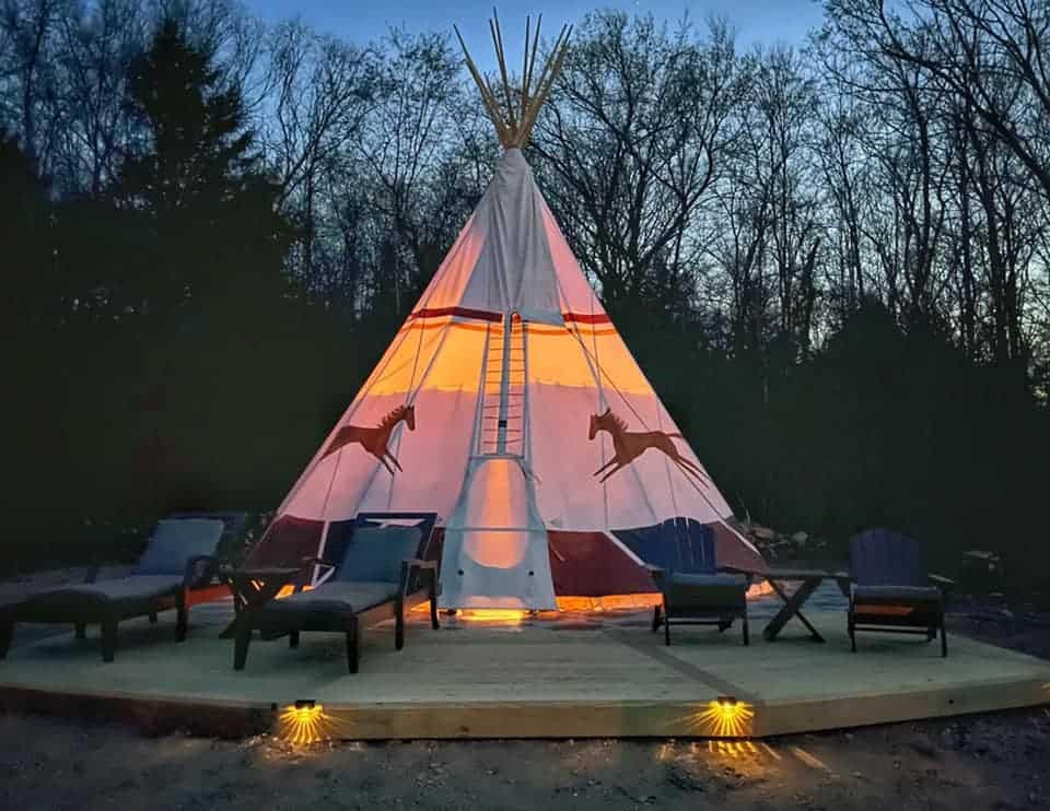 A teepee is lit up at night in a glamping site.