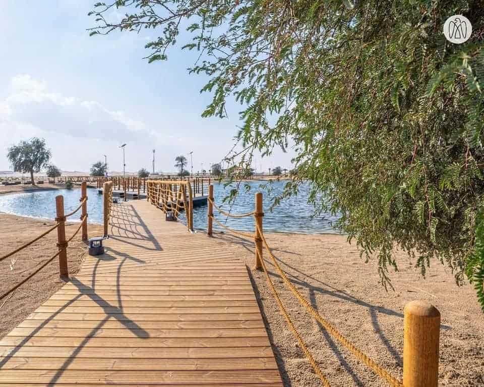 An eco-friendly wooden walkway leading to a lake in Abu Dhabi, an ideal camping destination.