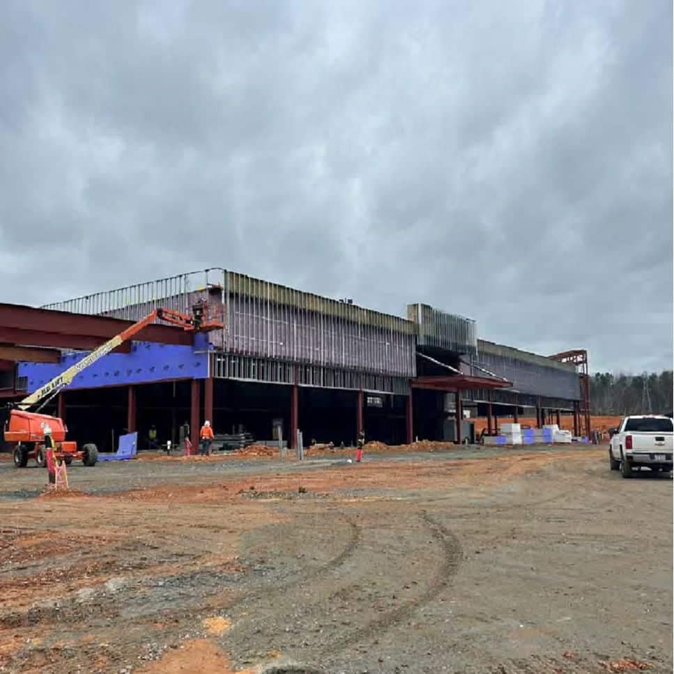 Construction site with workers, featuring a partially completed building with metal beams and an auto draft crane under a cloudy sky.