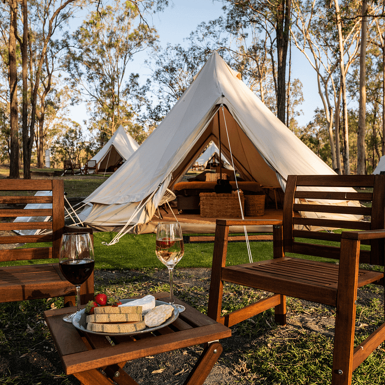 Guilderton Holiday Park's Glamping Offering features two chairs and a glass of wine in front of a tent.