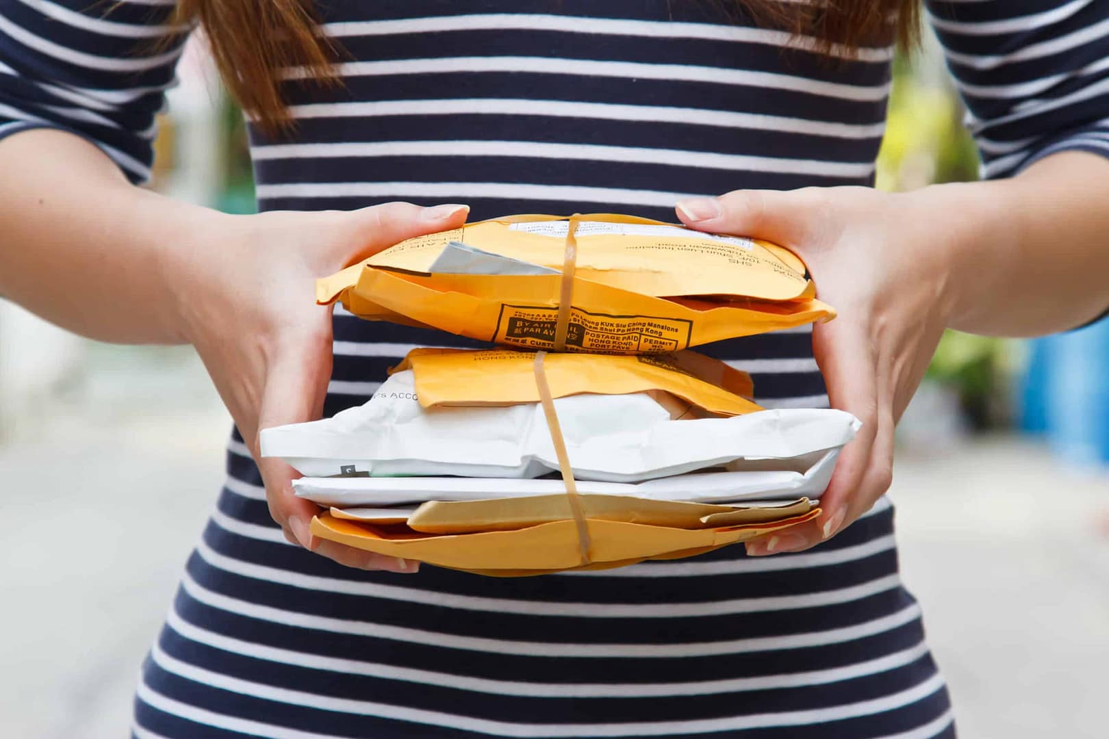 A person wearing a striped shirt holds a stack of small, yellow and white wrapped packages secured with a rubber band. The background is blurred.