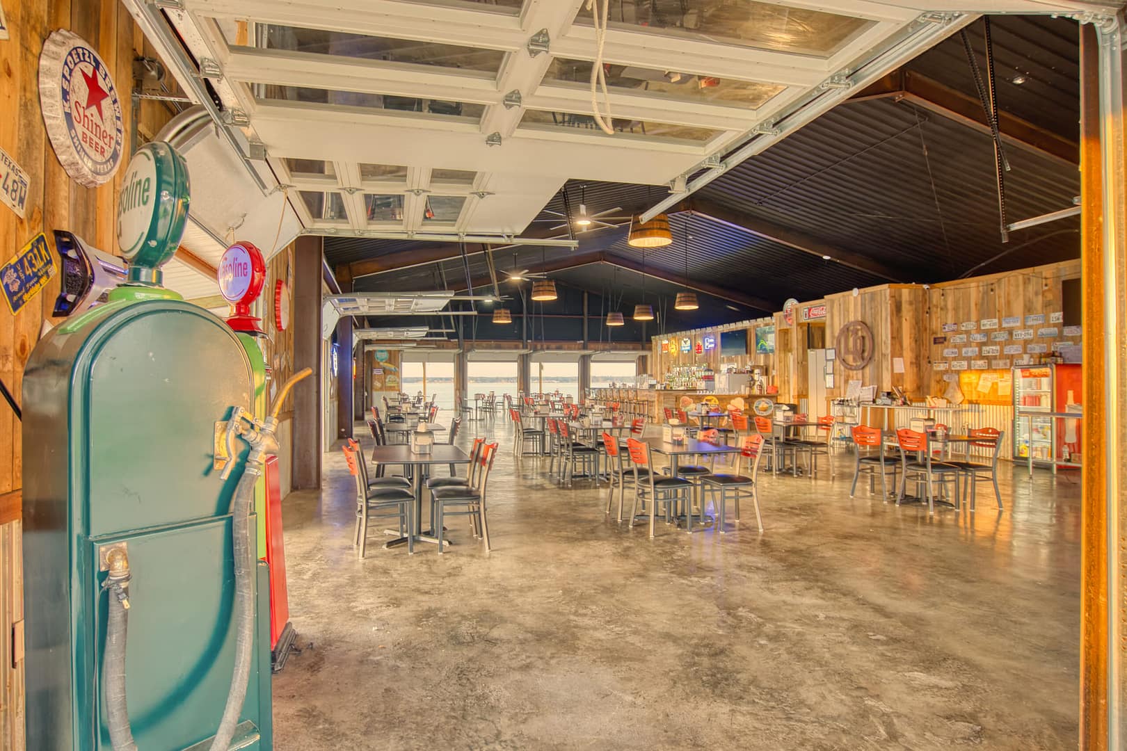 Spacious retro-themed restaurant with industrial decor, metal chairs and tables, exposed ceiling, neon signs, and vintage memorabilia on wood-paneled walls.