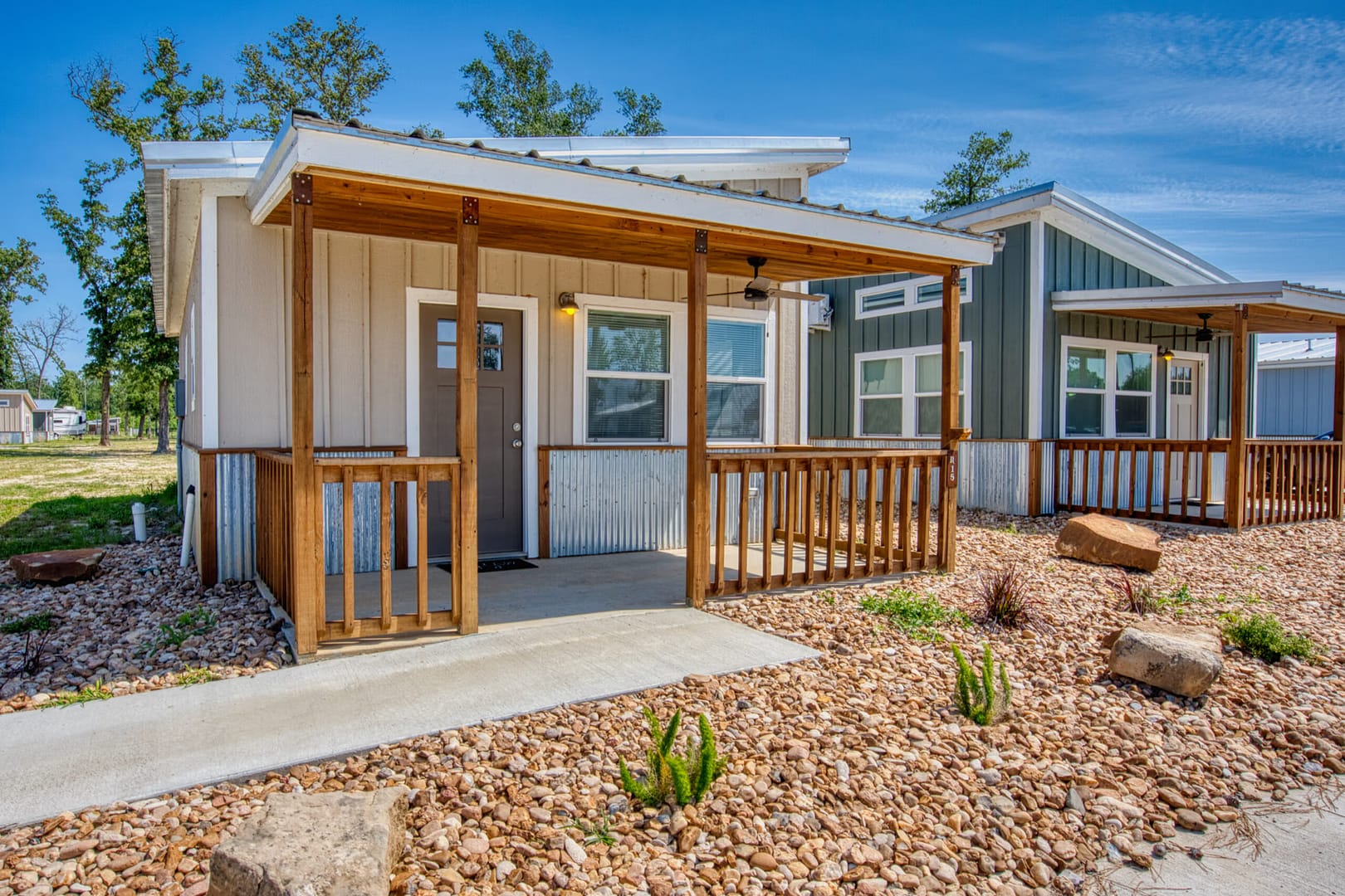 Small modern house with a metal roof, wooden porch, and gravel landscaping under a blue sky.